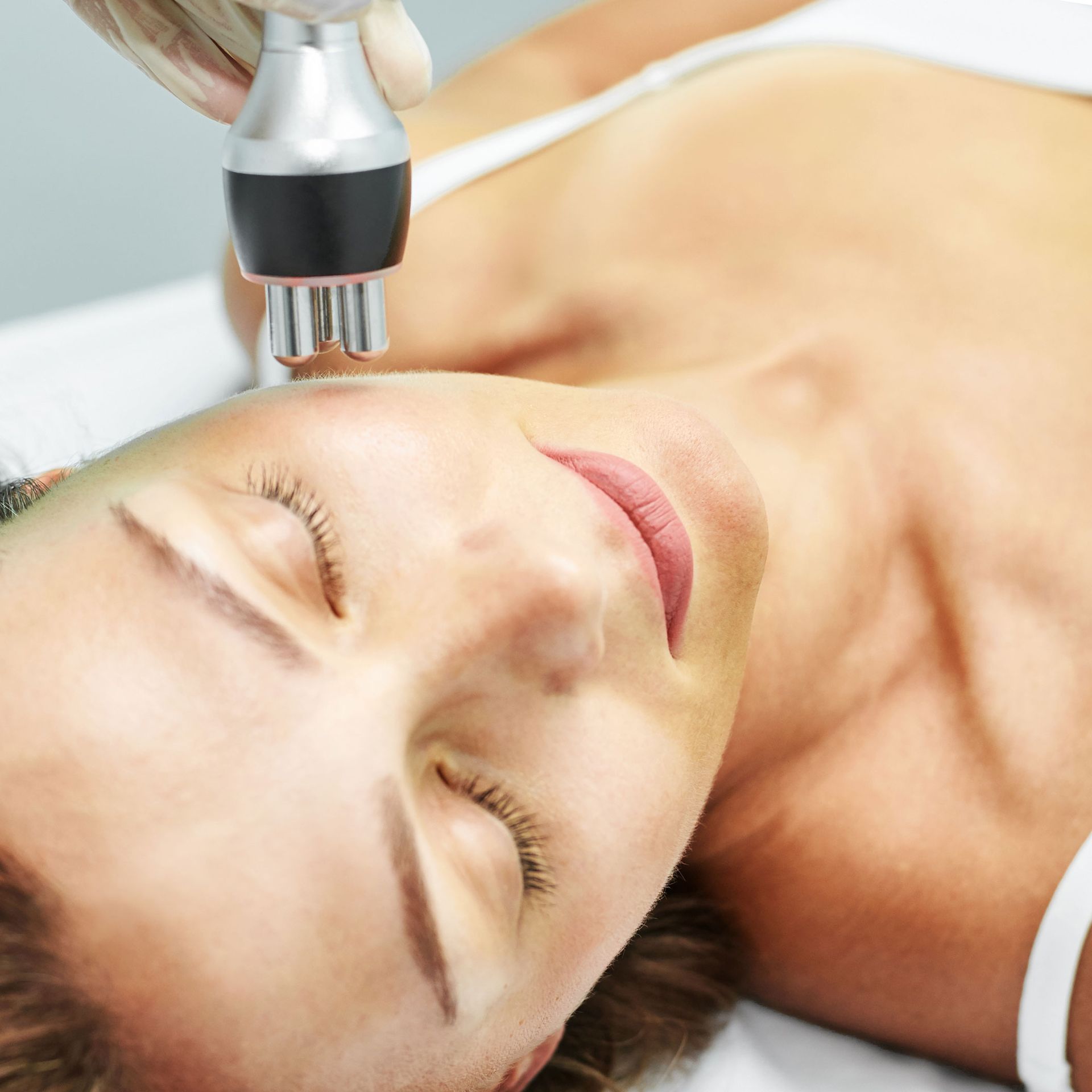 Woman receiving facial treatment; device on her forehead, eyes closed. Woman receiving facial treatment; device on her forehead, eyes closed.