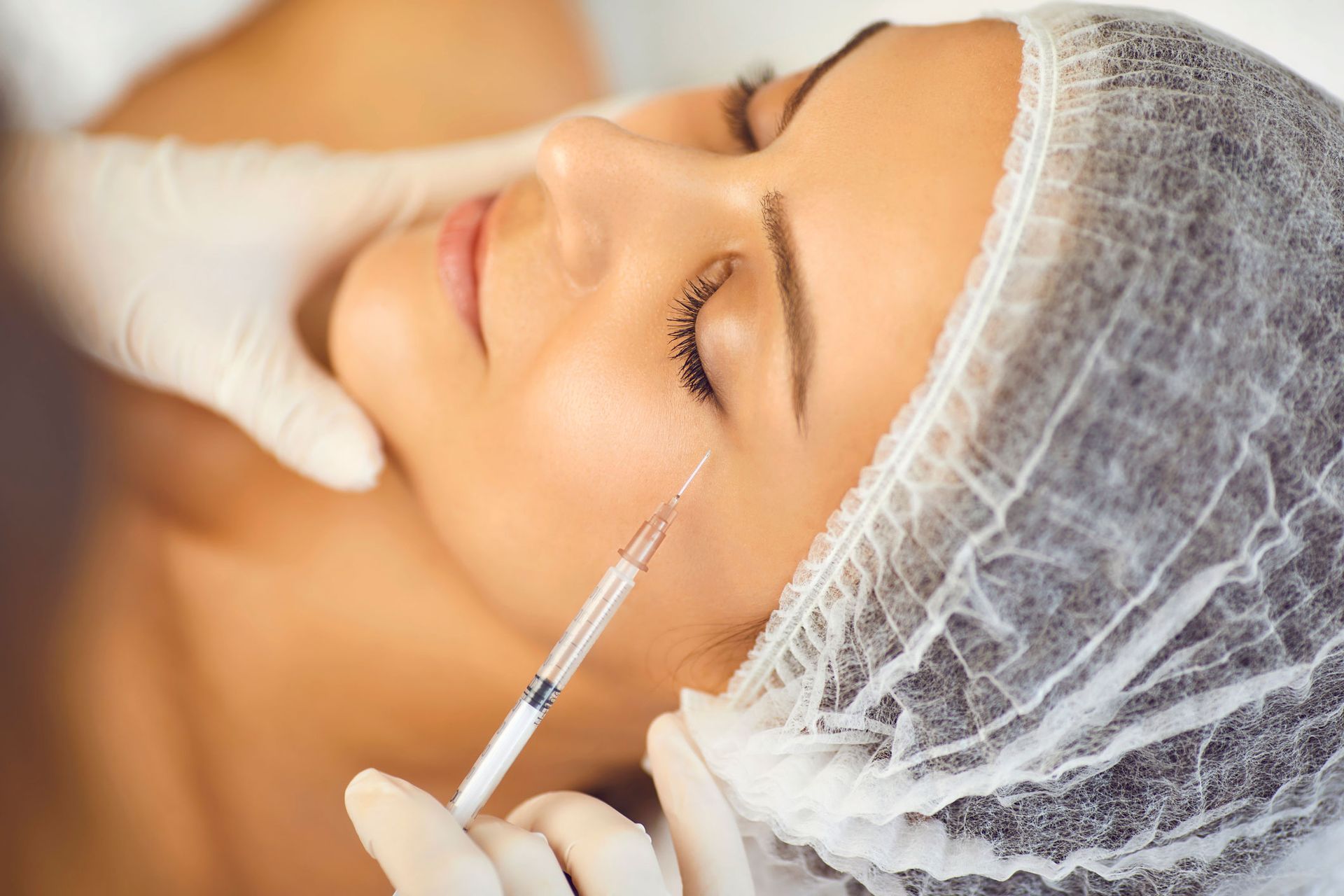 Person receiving a facial injection near the eye, in a medical setting.