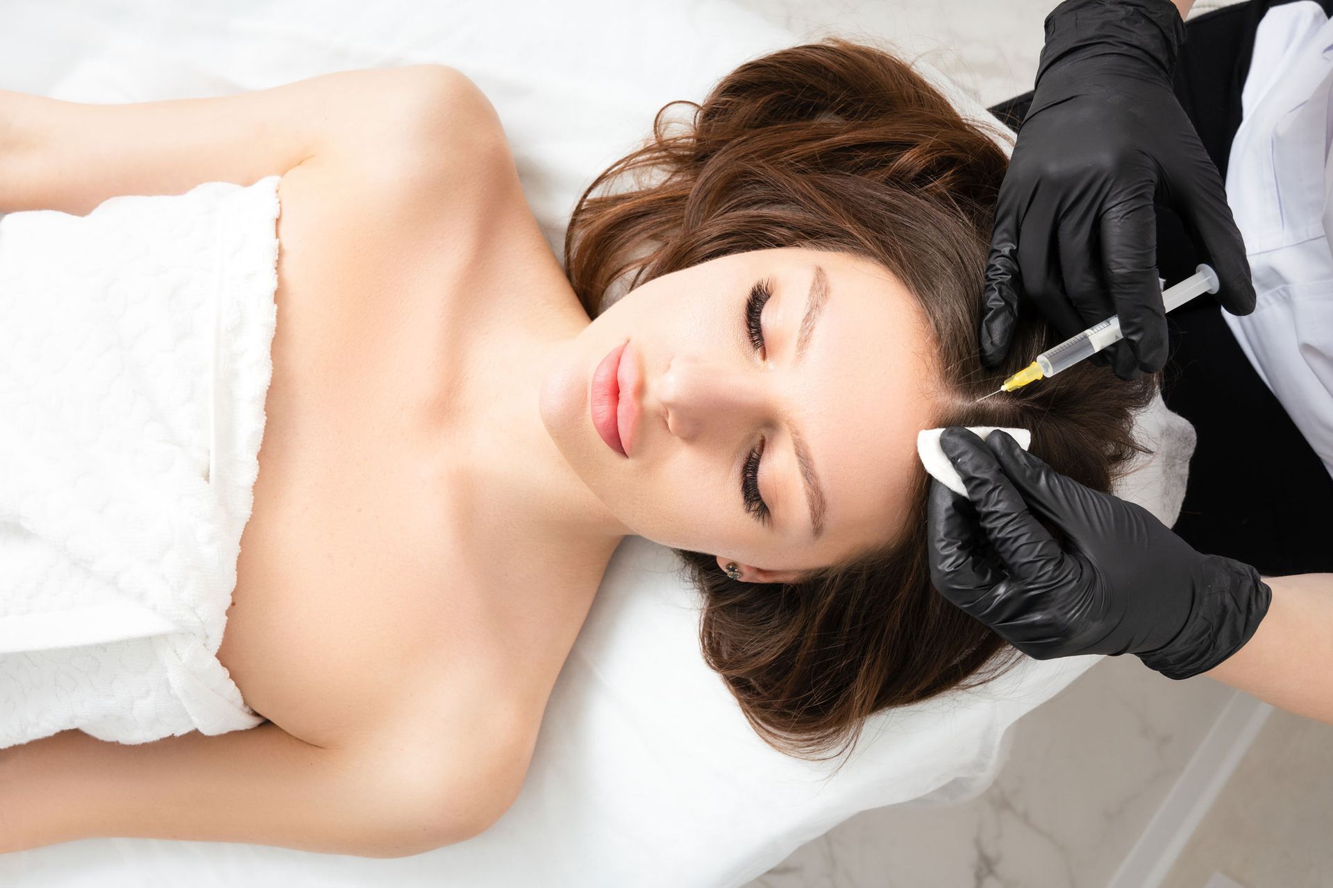Woman receiving a scalp injection; professional in black gloves administering treatment.