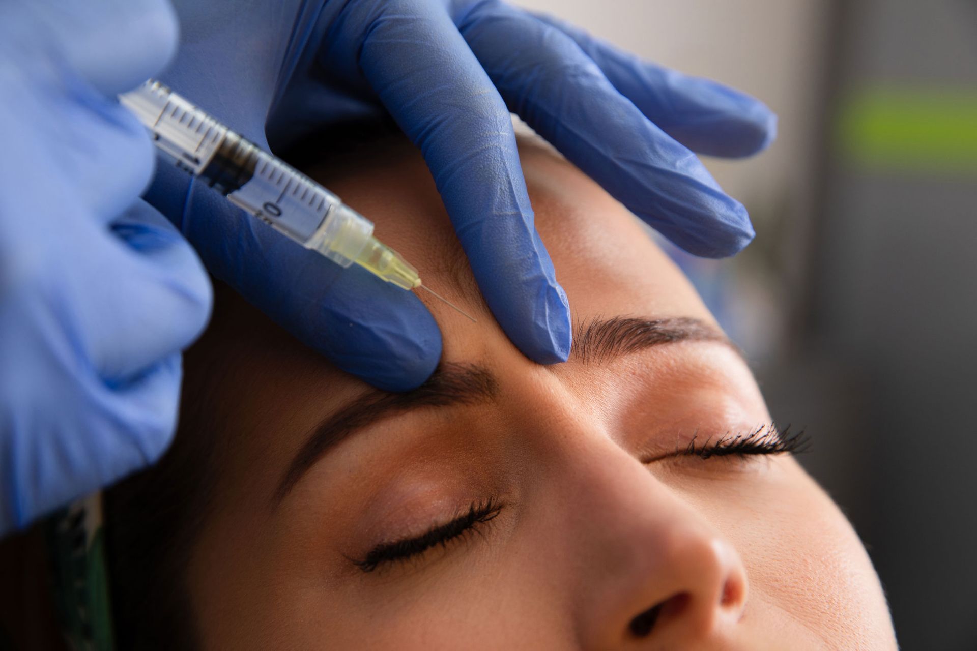 Gloved hand injecting brow. Woman with closed eyes receiving cosmetic procedure in clinic. Gloved hand injecting brow. Woman with closed eyes receiving cosmetic procedure in clinic.
