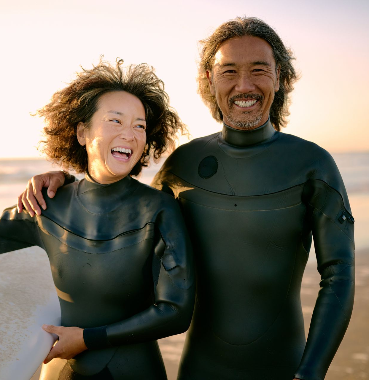 Wooden sign with Couple in wetsuits on beach, holding surfboard, smiling.