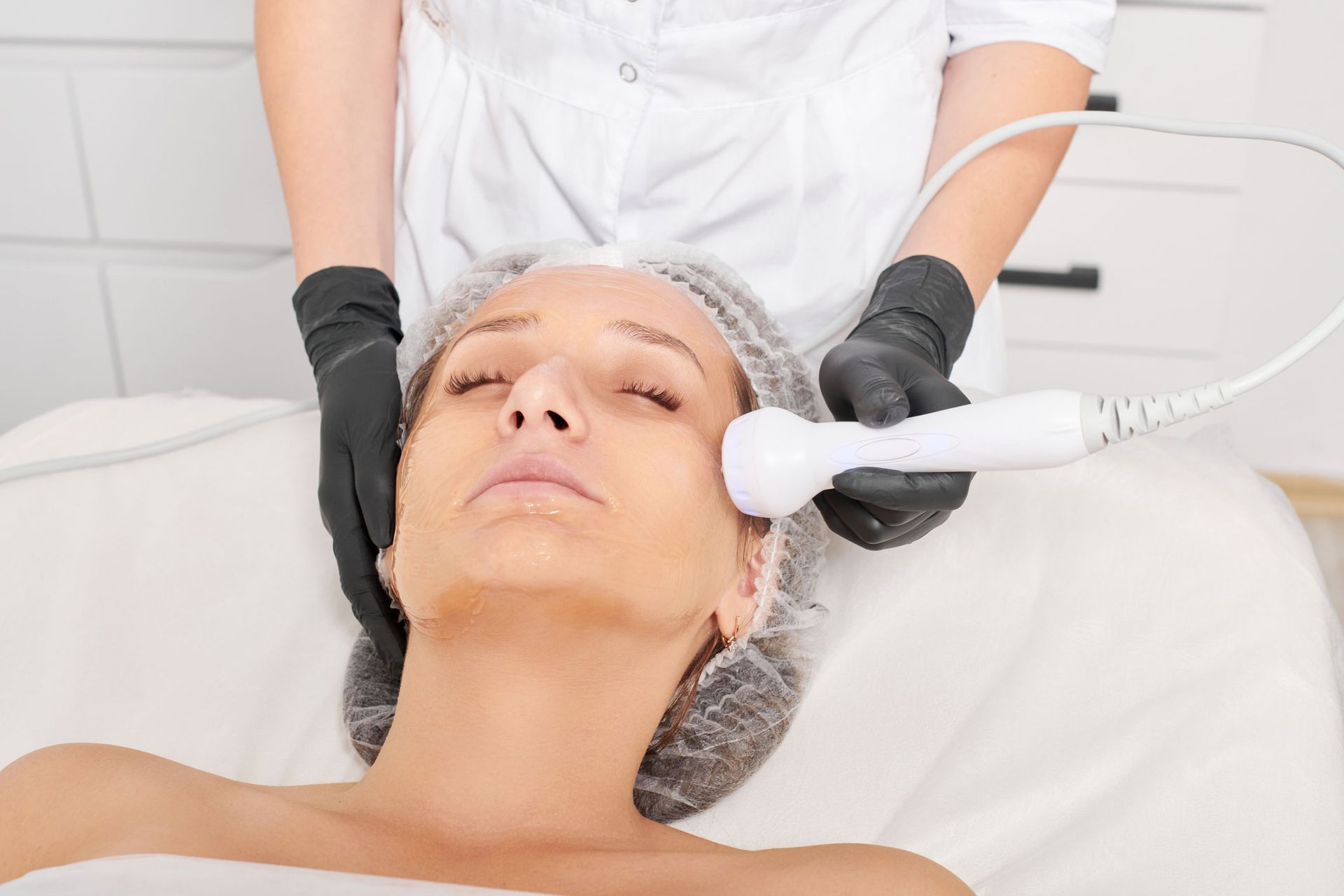 Woman receiving facial treatment in a spa, using a handheld device. Woman receiving facial treatment in a spa, using a handheld device.