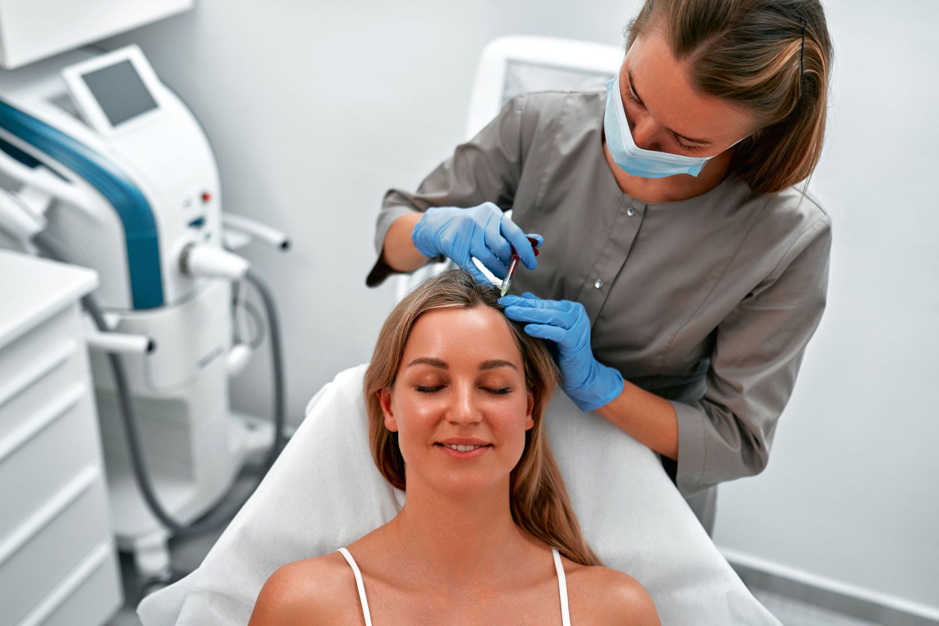 Woman receiving scalp injections in a medical setting. A clinician wearing gloves and a mask is administering the injections.