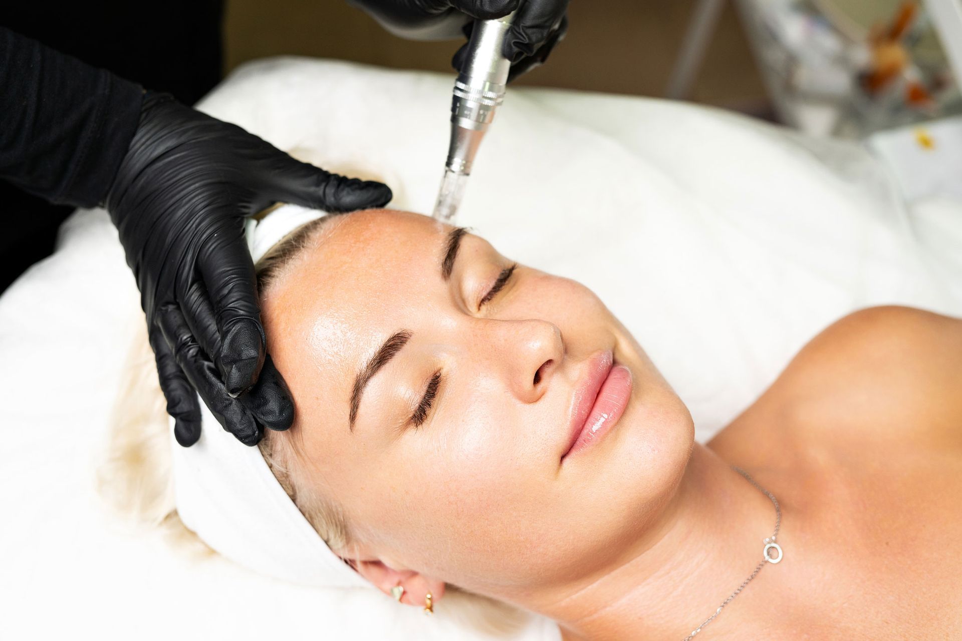 Person receiving a facial treatment; device held near forehead; black gloves; white sheet. Person receiving a facial treatment; device held near forehead; black gloves; white sheet.