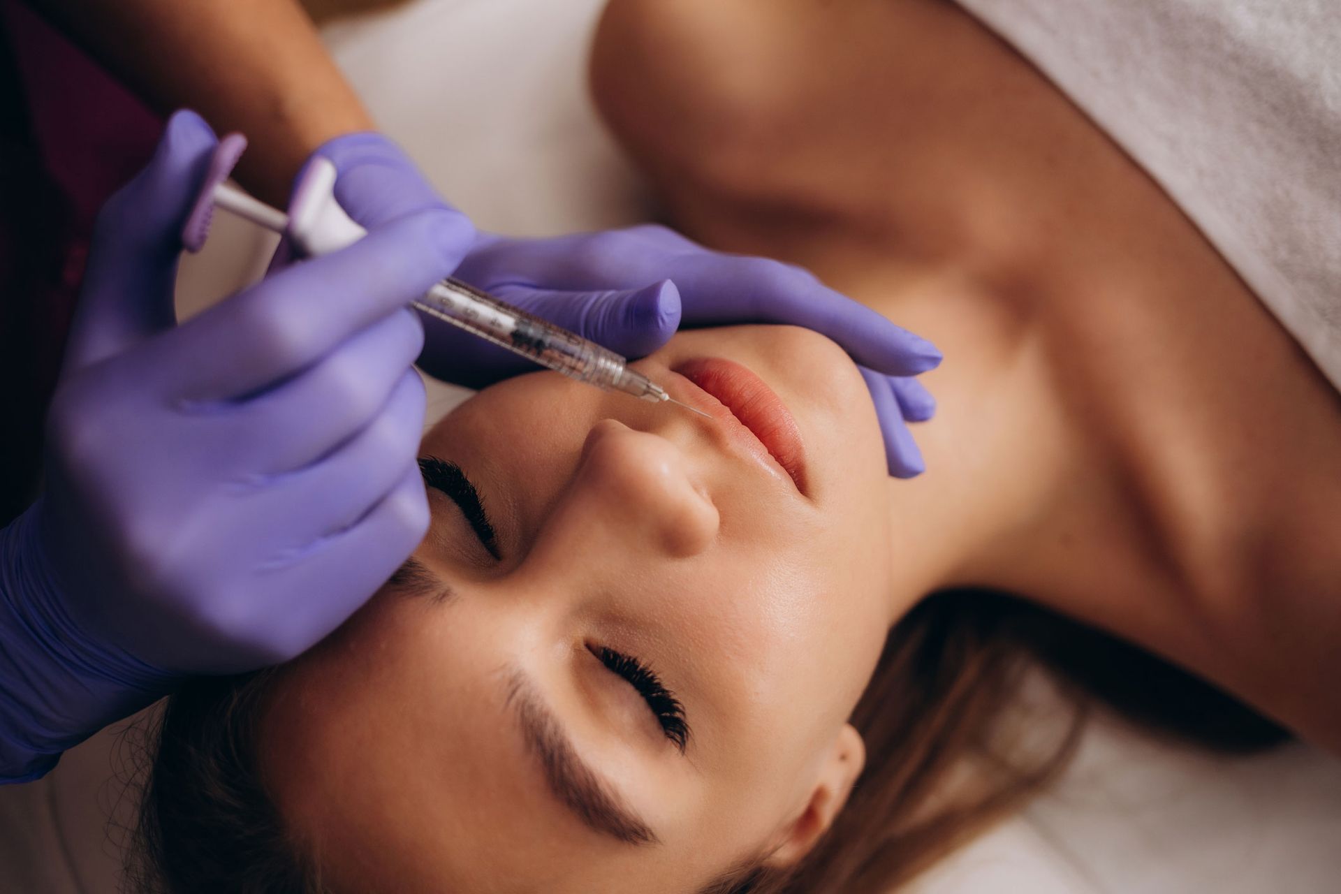 Person receiving lip filler injections. Hands in purple gloves, syringe near lips. Person receiving lip filler injections. Hands in purple gloves, syringe near lips.
