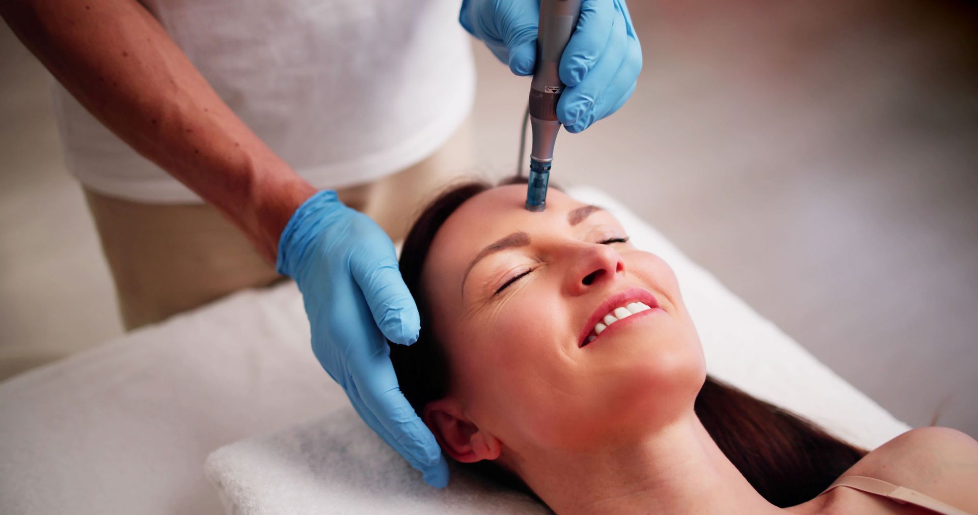 Person receiving facial treatment with tool on forehead. Smiling, light-skinned person in spa setting. Person receiving facial treatment with tool on forehead. Smiling, light-skinned person in spa setting.