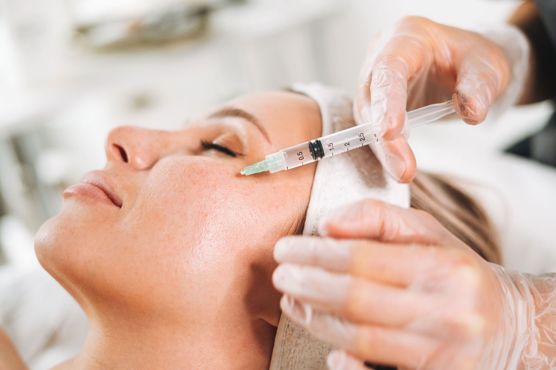Person receiving facial injection in a medical setting. A gloved hand injects the cheek near the eye. Person receiving facial injection in a medical setting. A gloved hand injects the cheek near the eye.