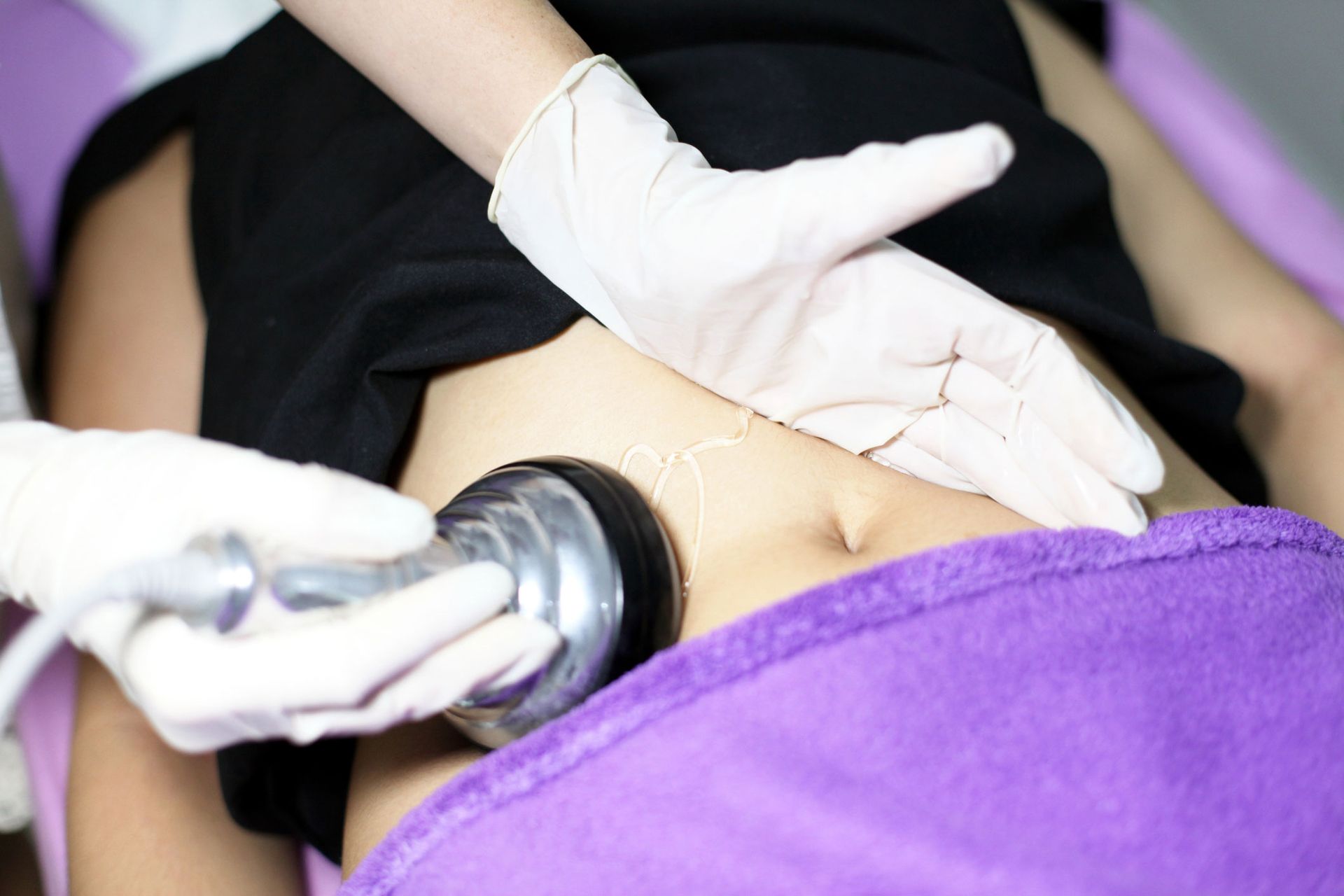 Hands wearing gloves using a device on a person's abdomen, on a treatment table. Hands wearing gloves using a device on a person's abdomen, on a treatment table.