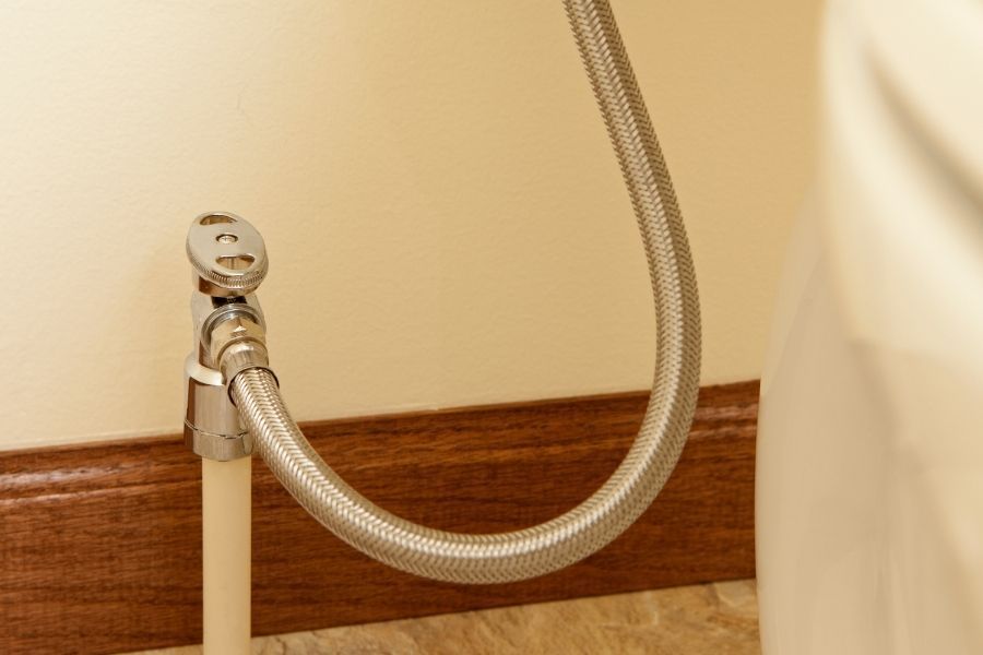 Close-up of a braided stainless steel toilet supply line connected to the base of a residential toilet
