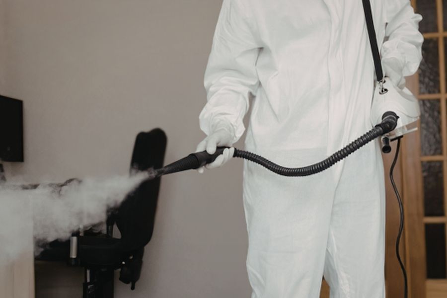 Technician in white protective coveralls and gloves fogging a room with a handheld sprayer wand in Tavares FL