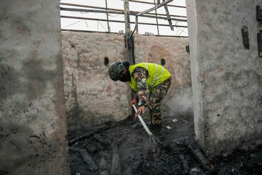 Worker in a high-visibility vest and respirator raking burned debris inside a fire damaged home in Central Florida