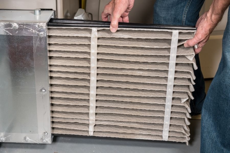 Hands sliding a clean pleated HVAC air filter into a metal furnace housing in a residential utility space
