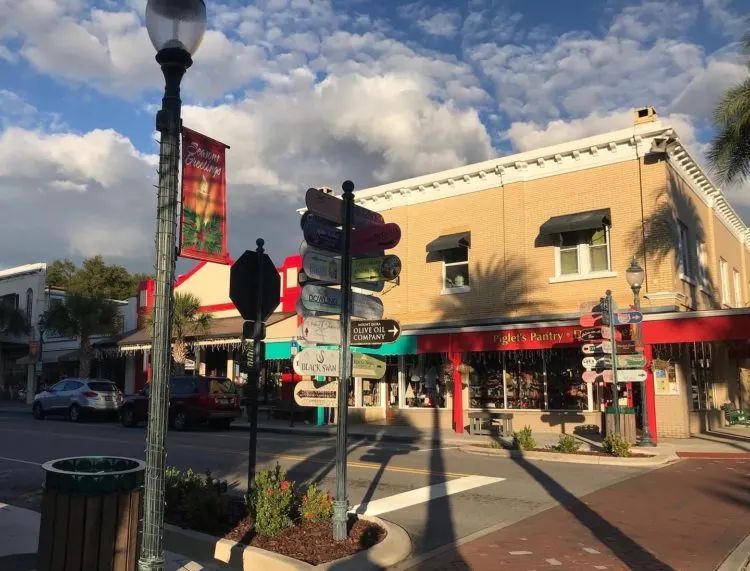 A sunny road view of Mount Dora, Florida, with a clear blue sky. A car is parked by the road, and a bustling café