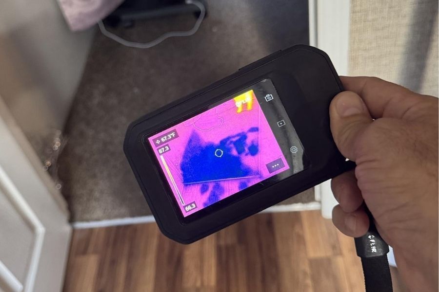 Technician using thermal imaging camera on a wall to trace hidden moisture from a pipe leak in a residential kitchen