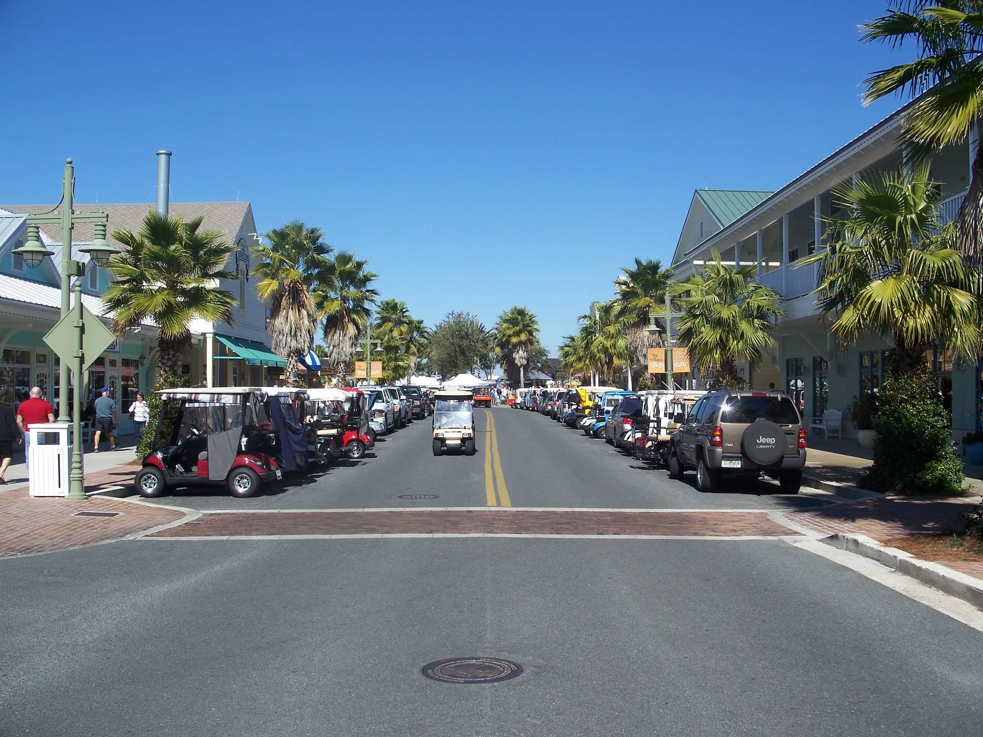 Sunny road view in The Villages with parked cars and palms.