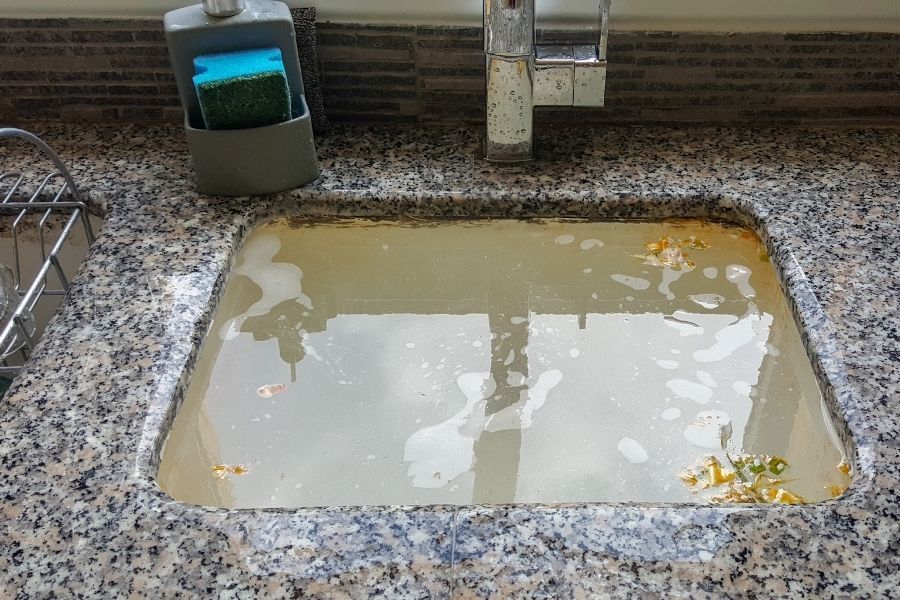 Clogged kitchen sink backed up with standing water, a common result of grease buildup in drain lines