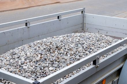 A utility trailer bed filled with gray gravel and secured by metal side rails.