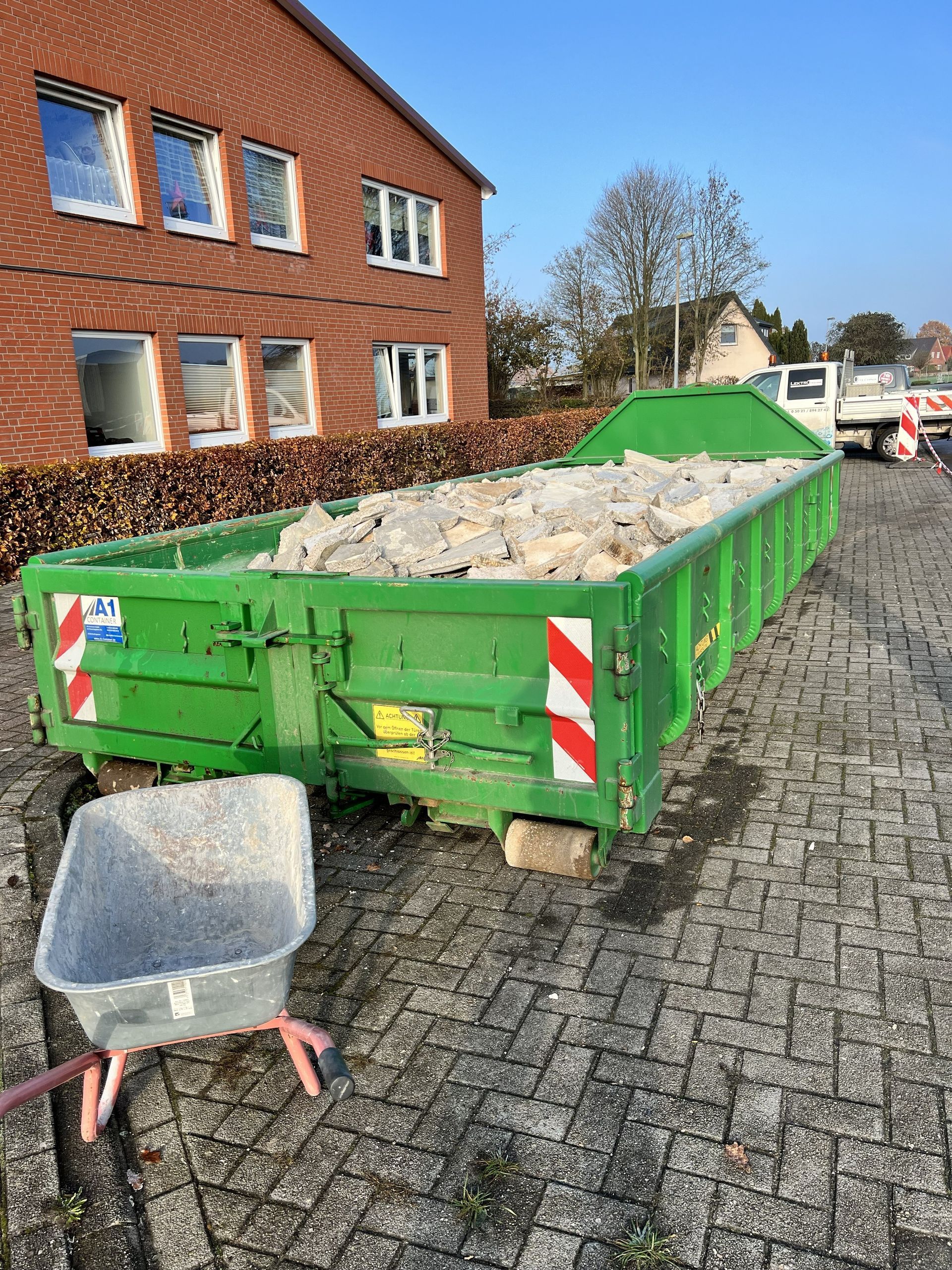 Green construction dumpster filled with rubble on a brick street beside a brick building
