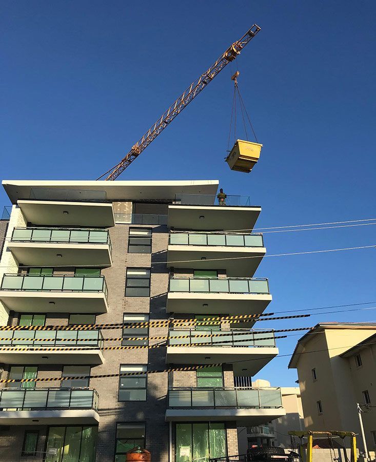 A Building Under Construction With A Crane Lifting A Skip Bin — Sunny's Skips in Wauchope, NSW