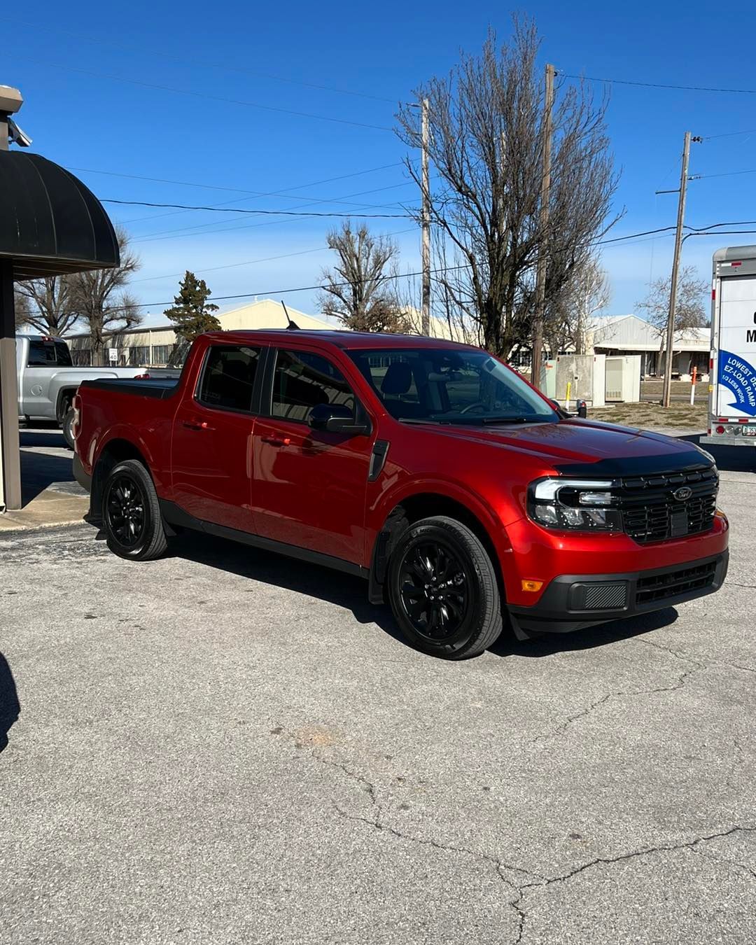 Red Ford Maverick truck with black accents parked on asphalt. Clear, sunny day.