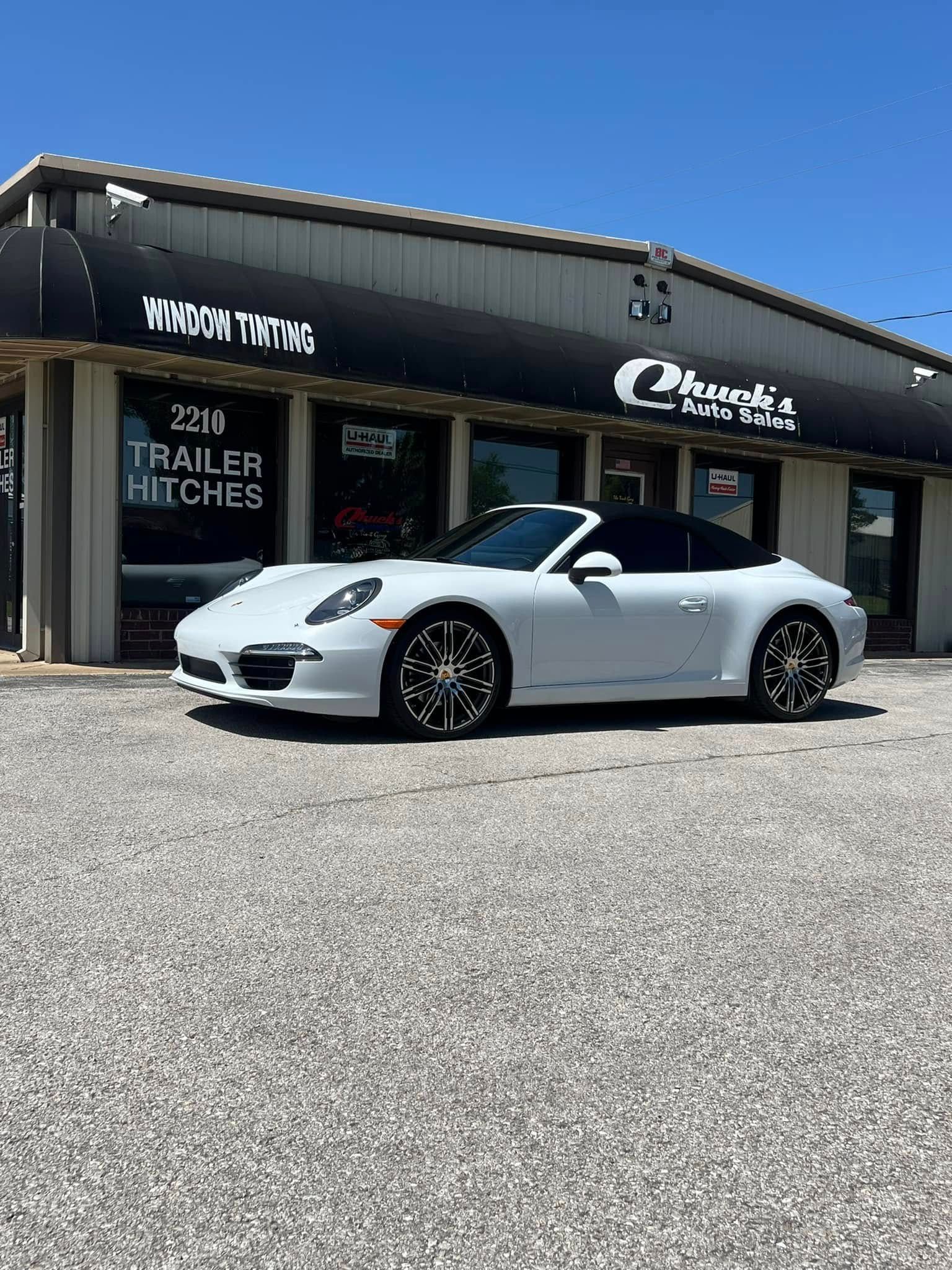 White Porsche convertible parked in front of a building with a black awning; sunny day.