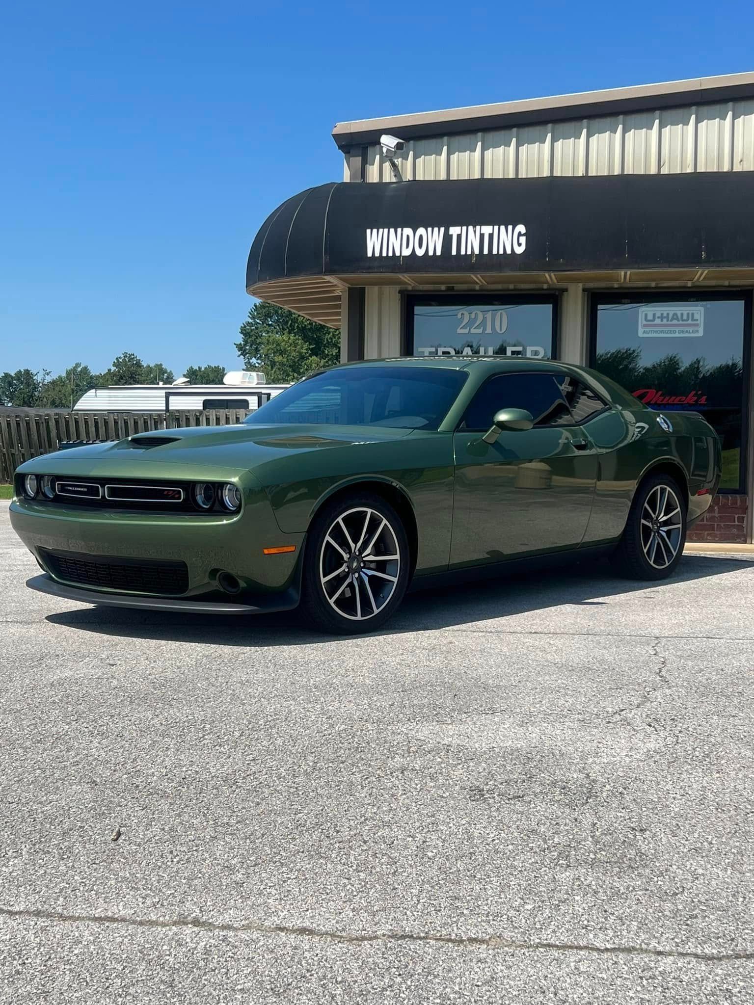 Green Dodge Challenger parked in front of a window tinting shop on a sunny day.