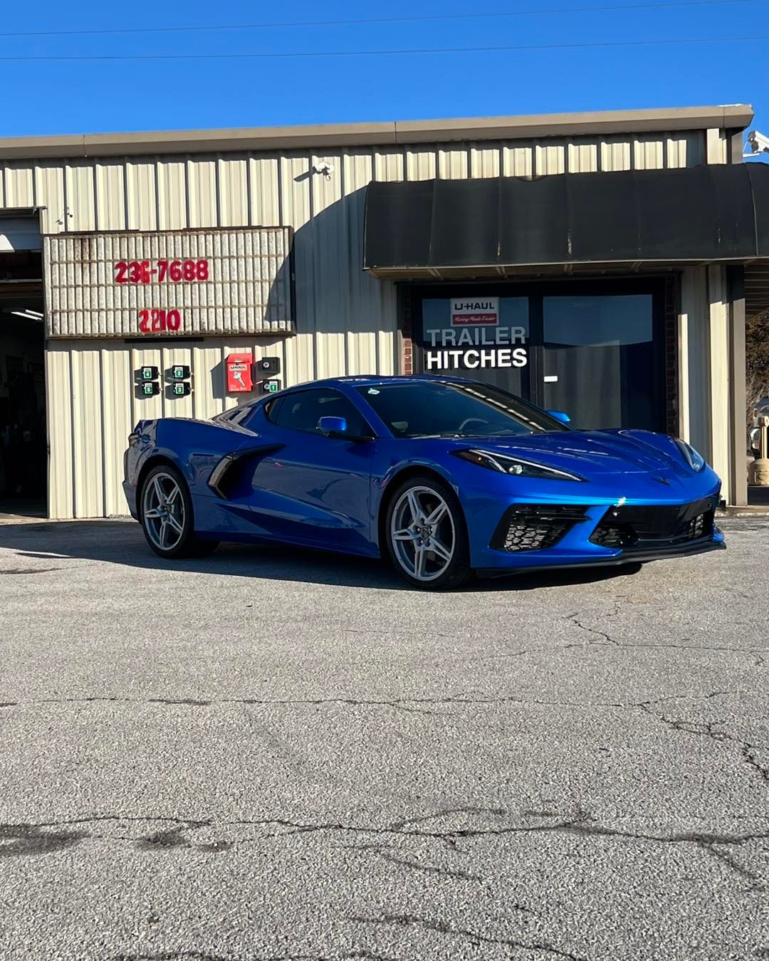 Blue sports car parked in front of a building with trailer hitches sign. Sunny day.