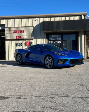 Blue sports car parked in front of a building with trailer hitches sign. Sunny day.
