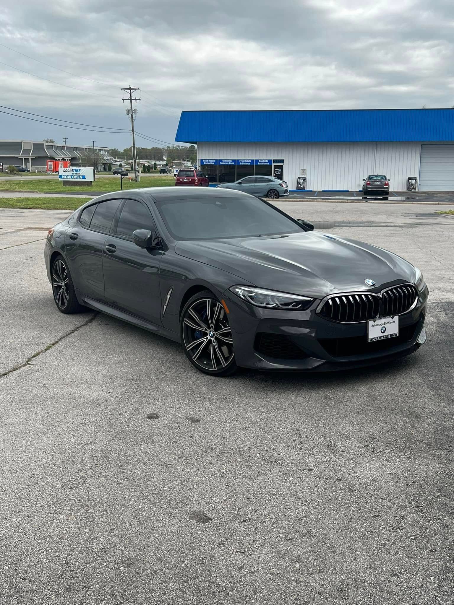 Gray BMW sedan parked in front of a building with a blue roof, under a cloudy sky.