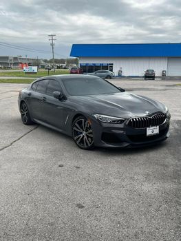 Gray BMW sedan parked in front of a building with a blue roof, under a cloudy sky.