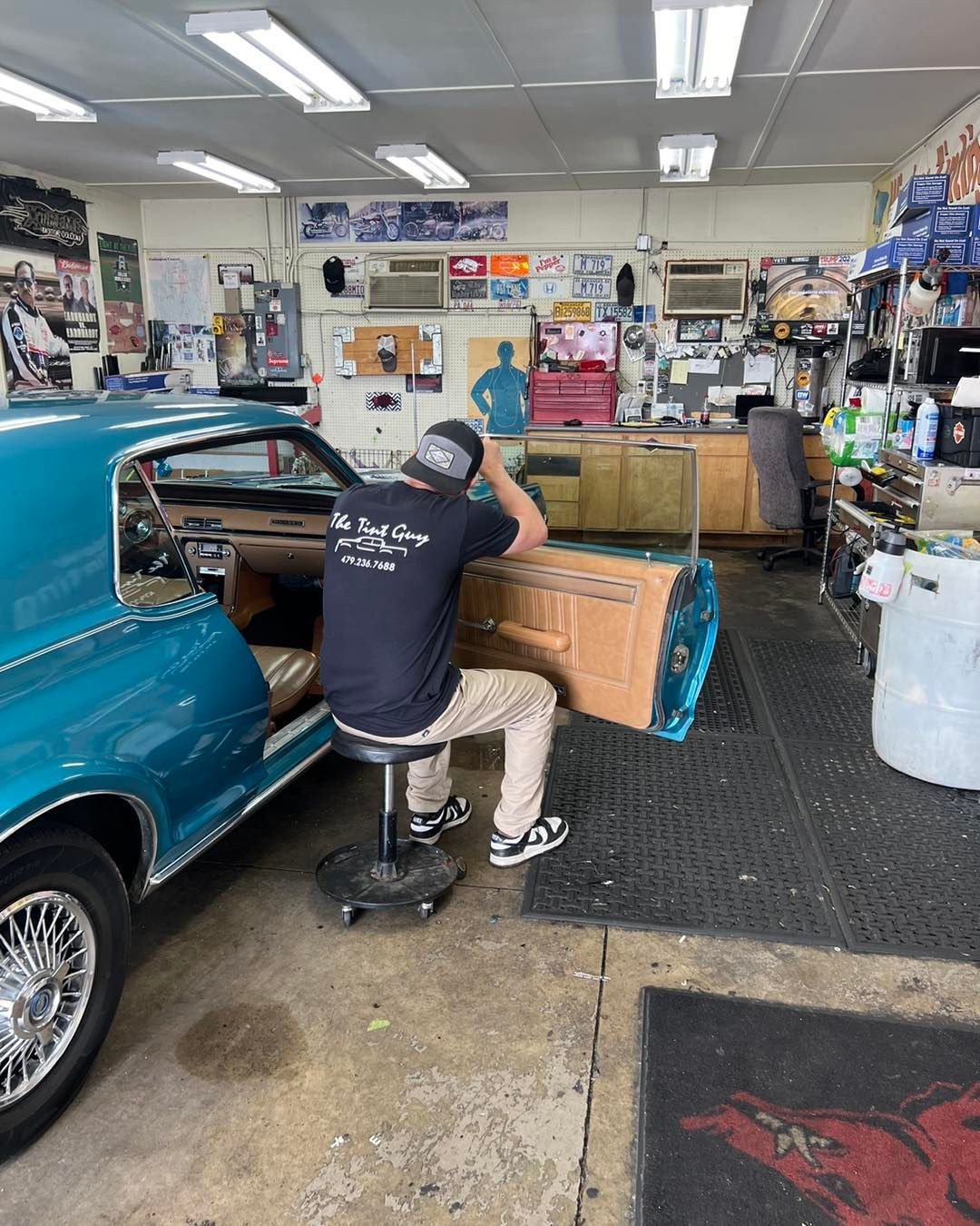 A person working on the door of a teal classic car in a shop.