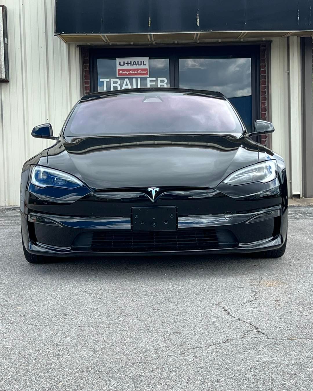 Black Tesla car parked in front of a U-Haul store.