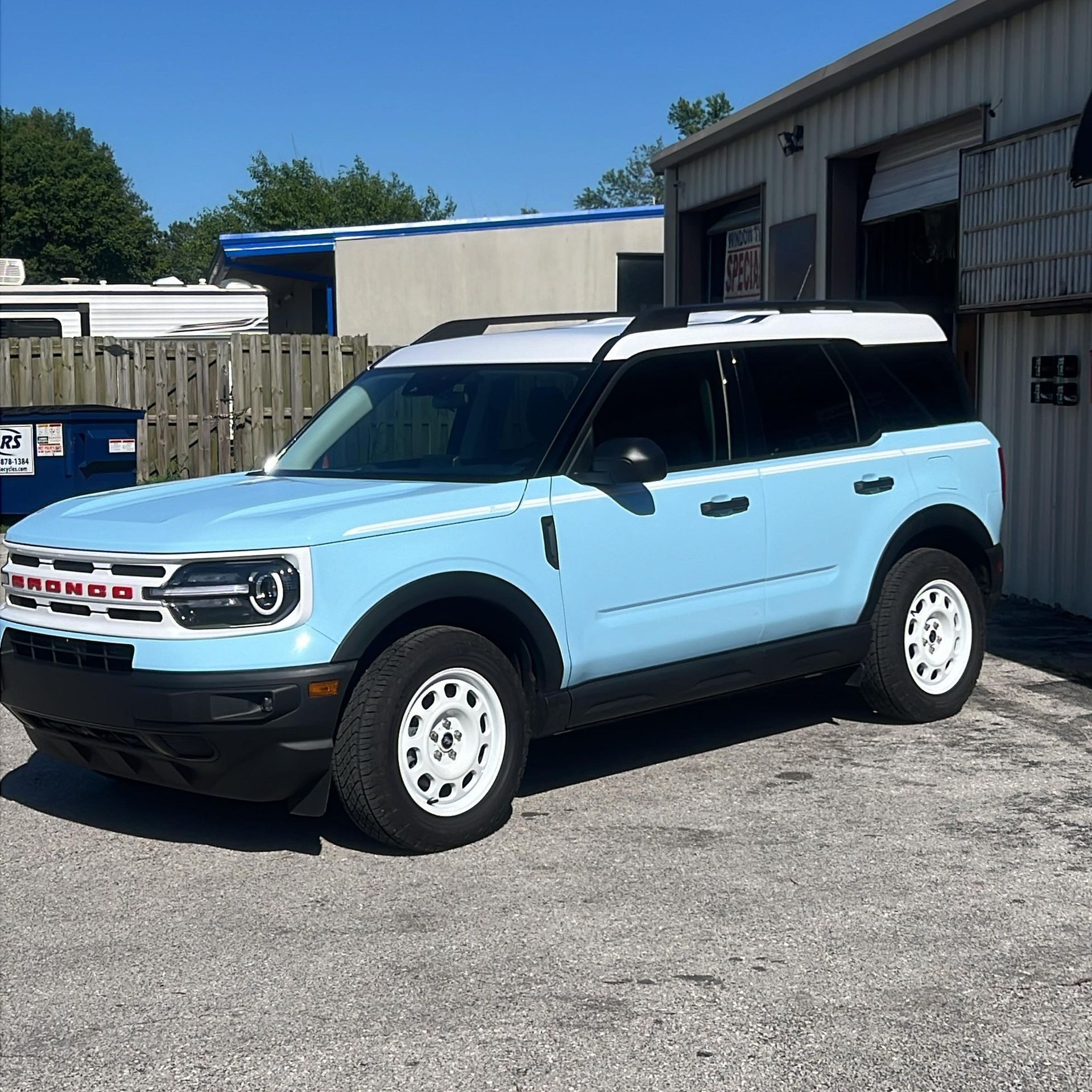 Light blue Ford Bronco Sport with white roof and wheels, parked near a garage.