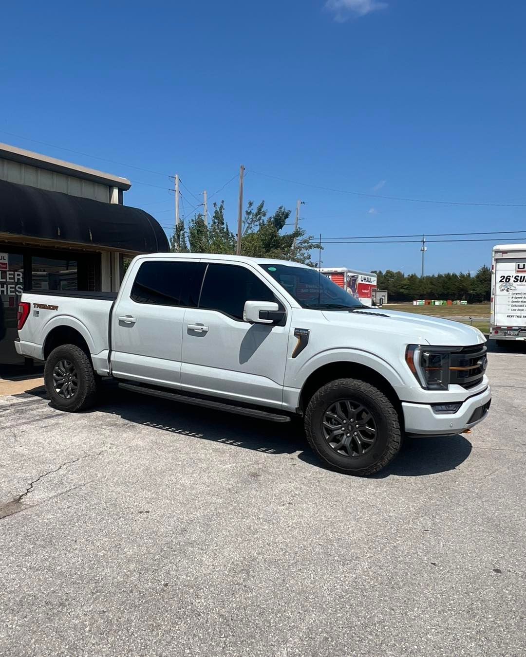 White Ford F-150 pickup truck parked on concrete, tinted windows, black wheels, sunny day.