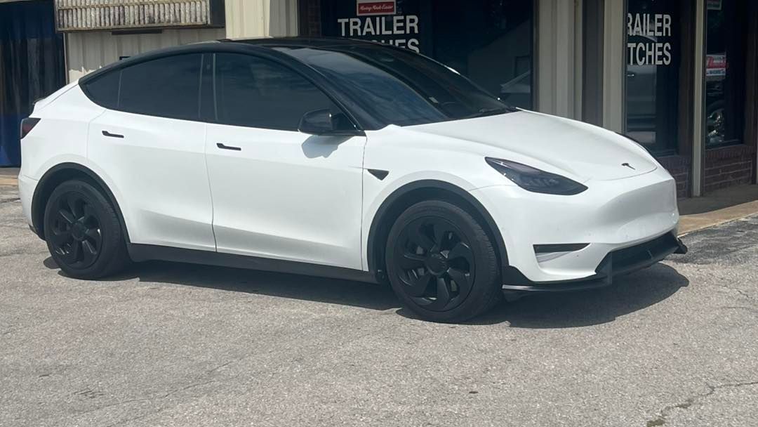 White Tesla Model Y with black roof and wheels parked outside a building.