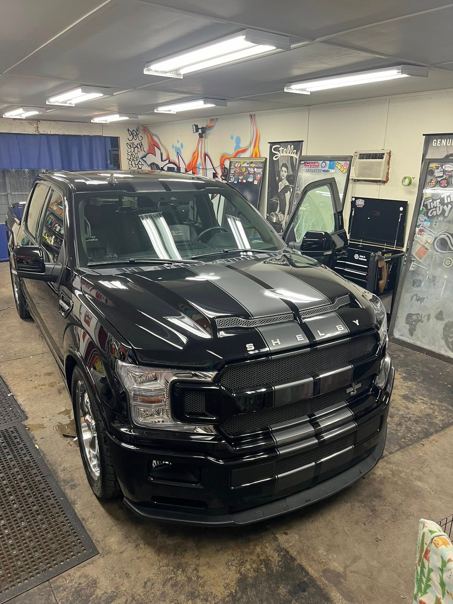 Black Ford F-150 truck with racing stripes parked inside a garage. The door is open.