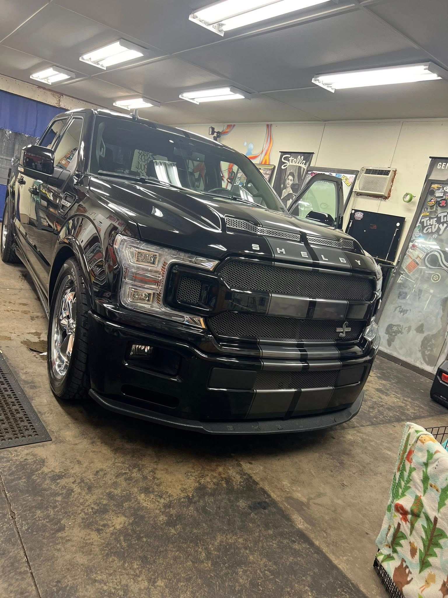 Black Ford pickup truck in a shop, with a racing stripe and custom grill.
