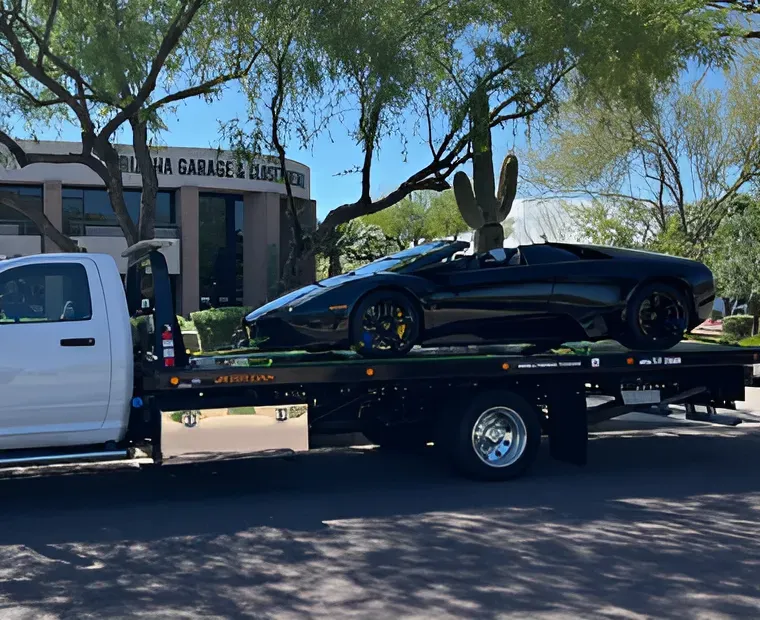 Black sports car on a flatbed tow truck parked on a sunny street near palm trees.
