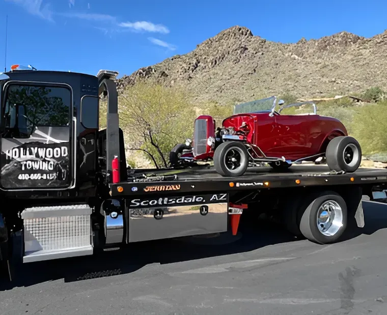 Red vintage hot rod on a flatbed tow truck in the desert sun.