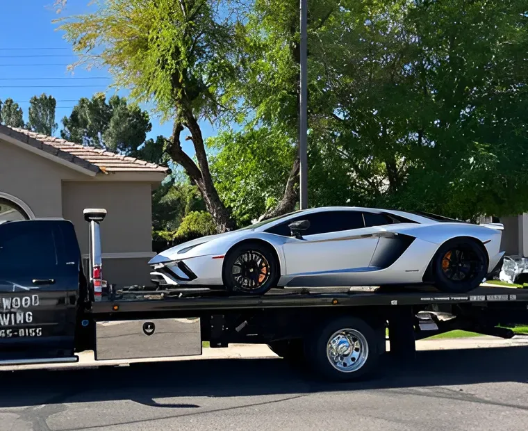 White sports car loaded on a black tow truck in a sunny residential driveway.