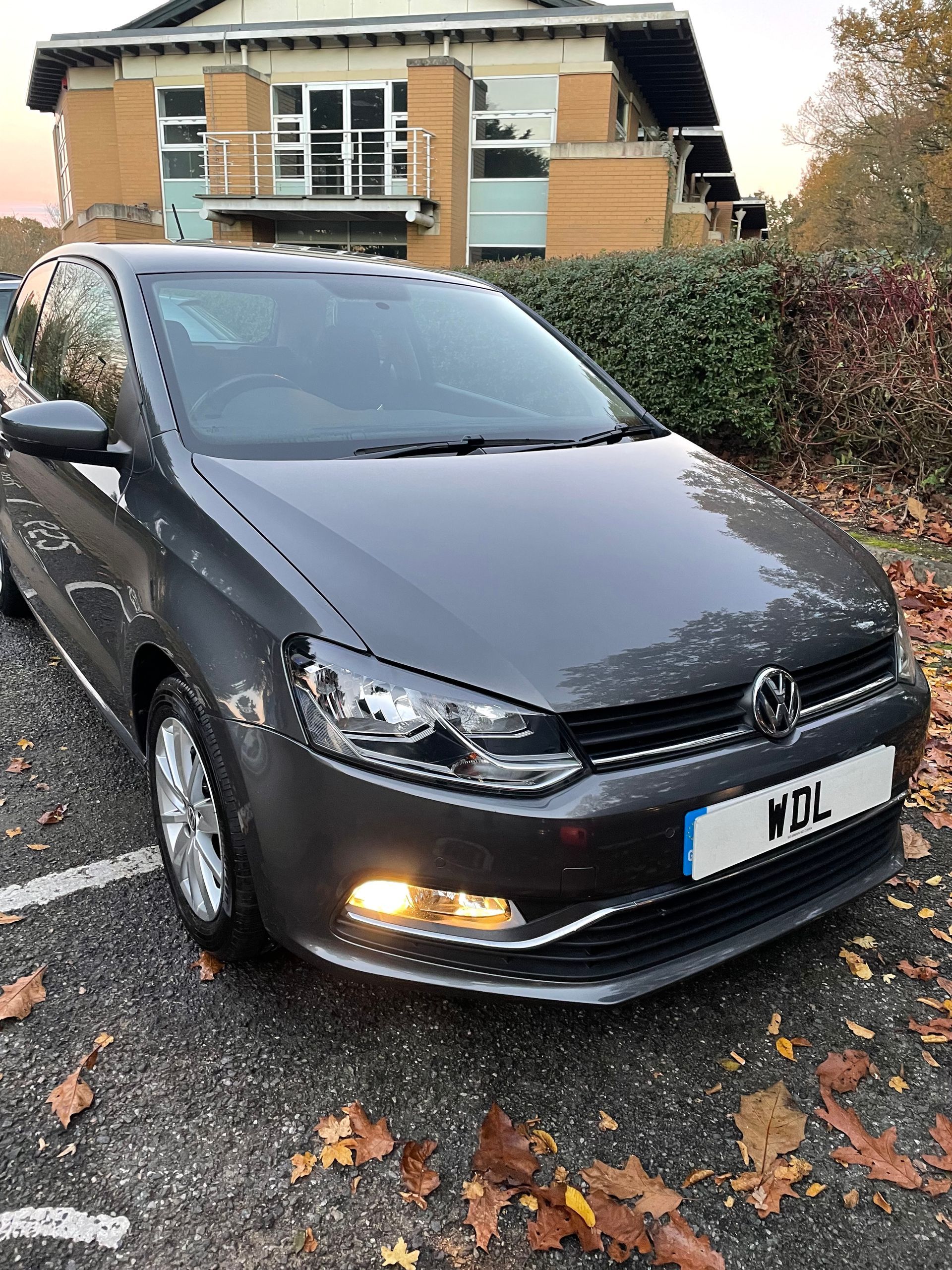 A volkswagen polo is parked in a parking lot in front of a building.