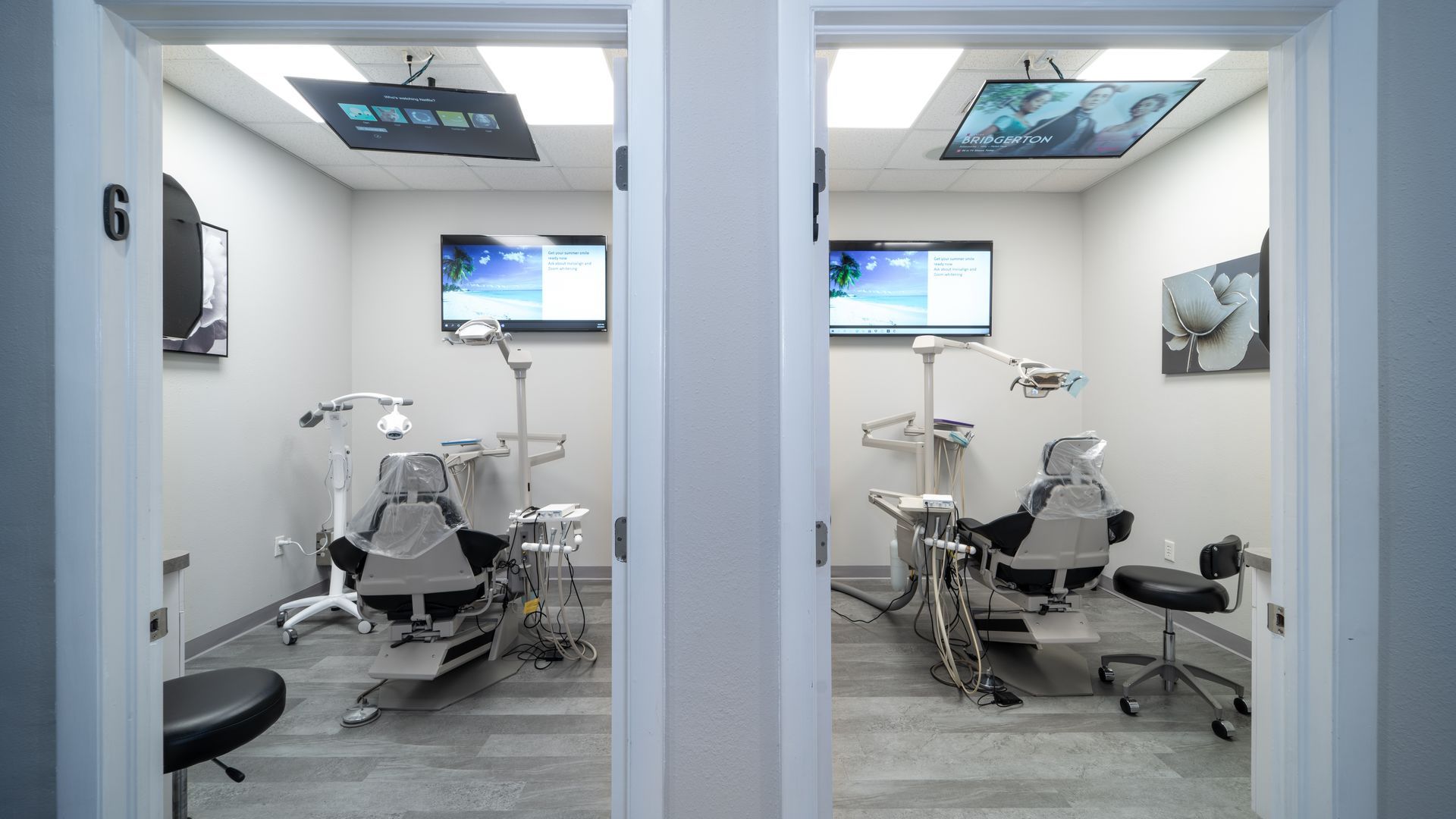 A dental office with two dental chairs and two televisions.