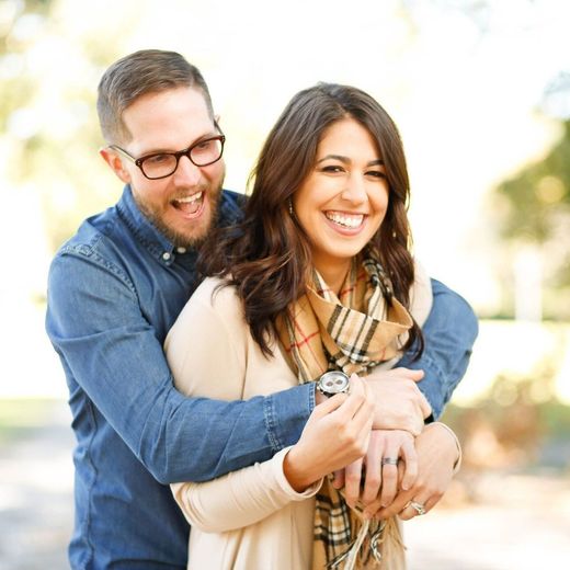 A man in glasses is hugging a woman in a plaid scarf