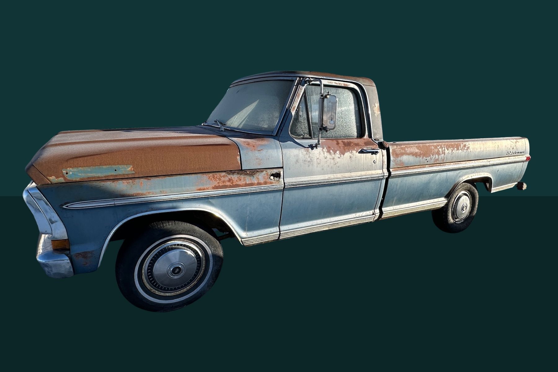 A rusty, blue and brown vintage pickup truck with flat tires, sitting on a green background.