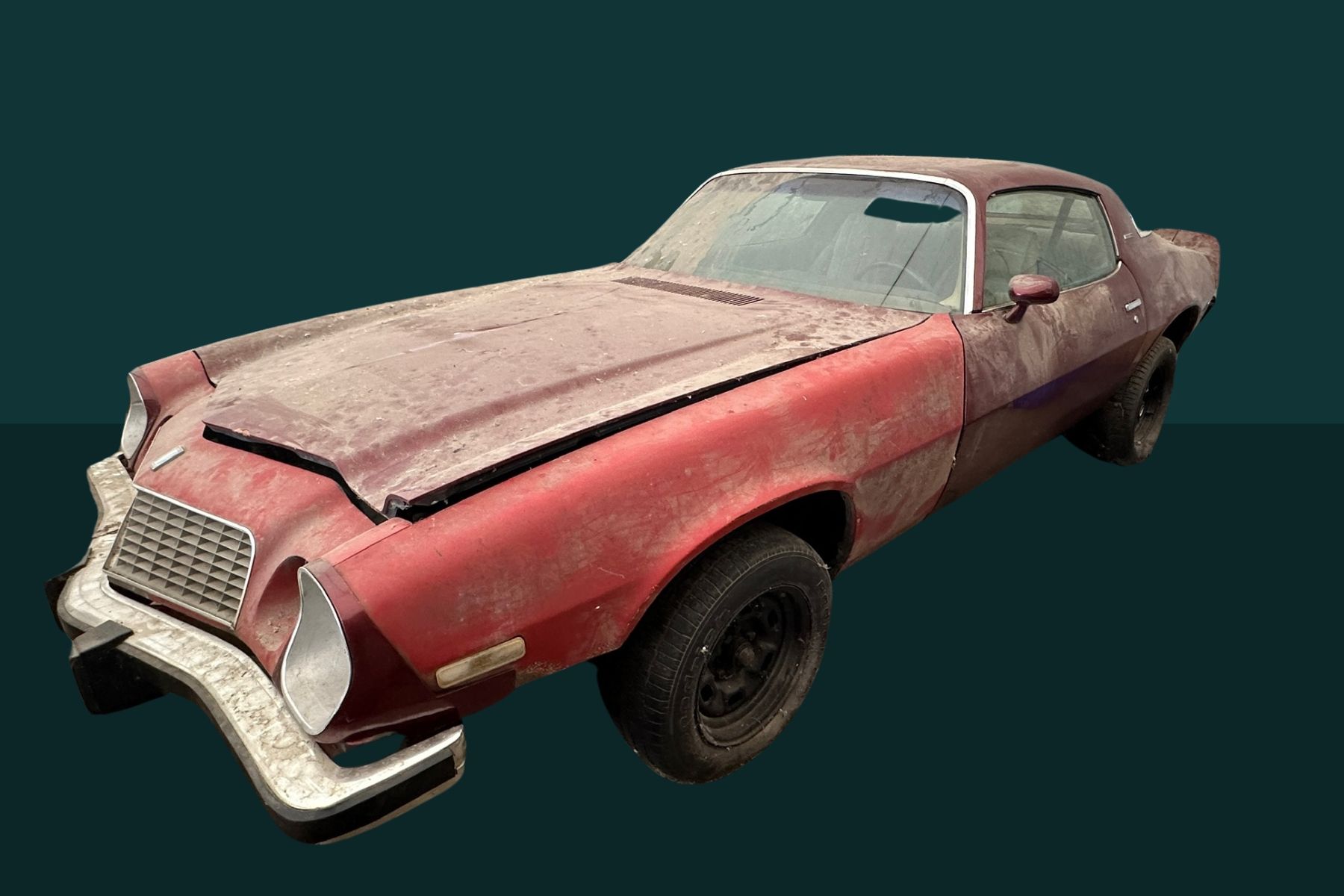 A rusty, red, older model Camaro car in disrepair, with a damaged front bumper and hood, sitting against a dark green background.