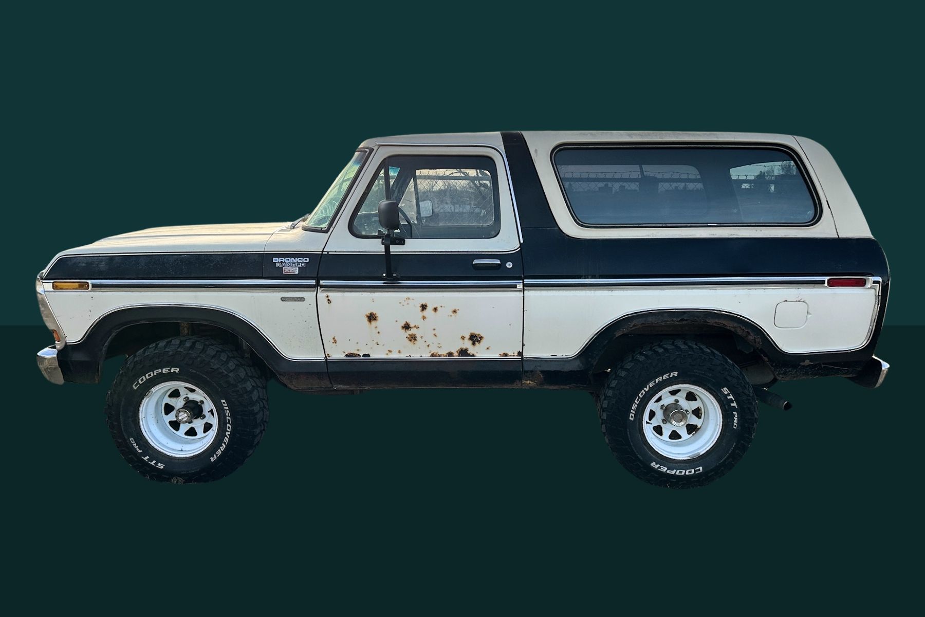 White and blue vintage Ford Bronco with rusted panels, set against a dark green background.