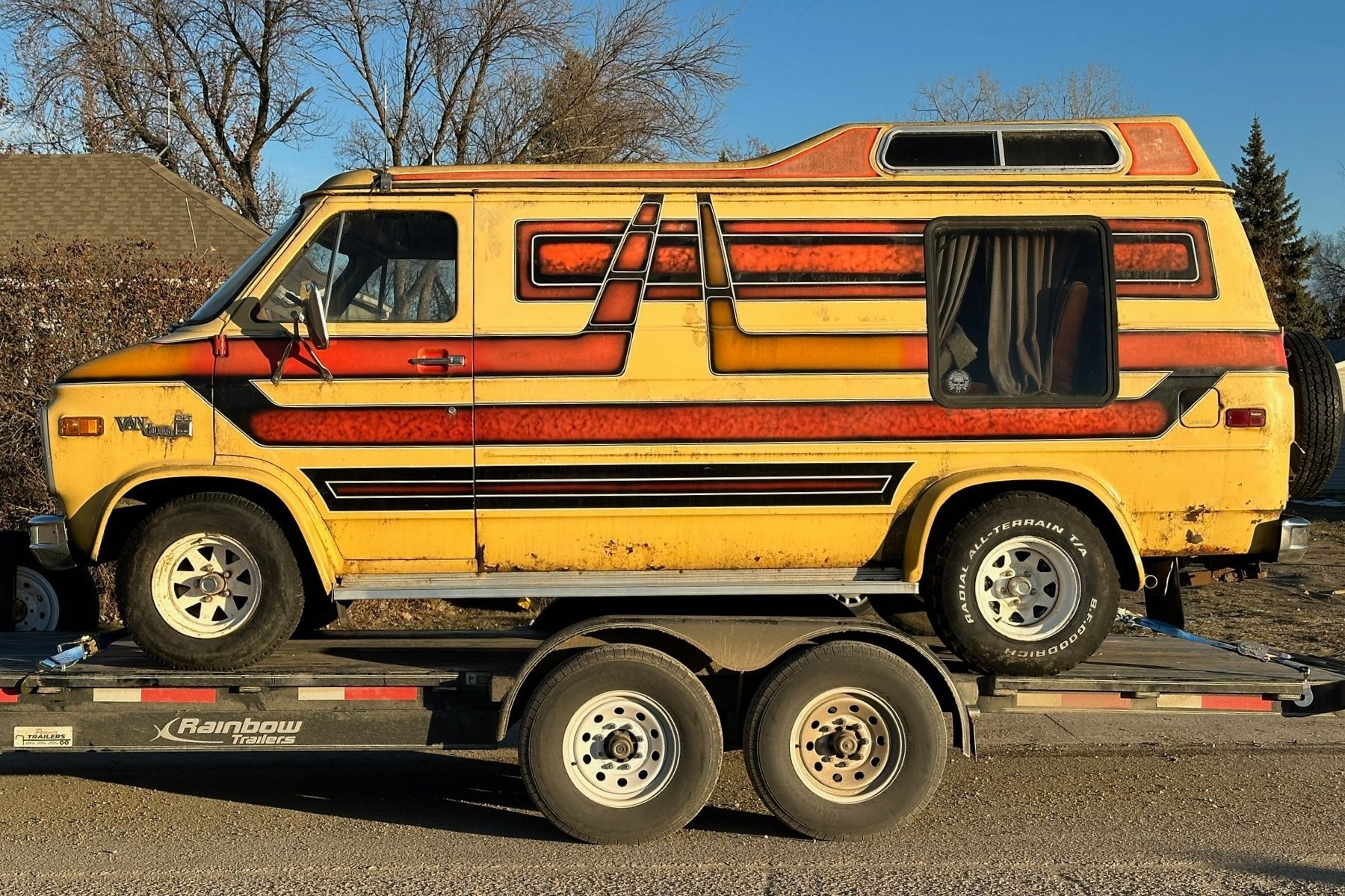 Yellow van with red and black stripes parked on a trailer outdoors, under a clear sky.