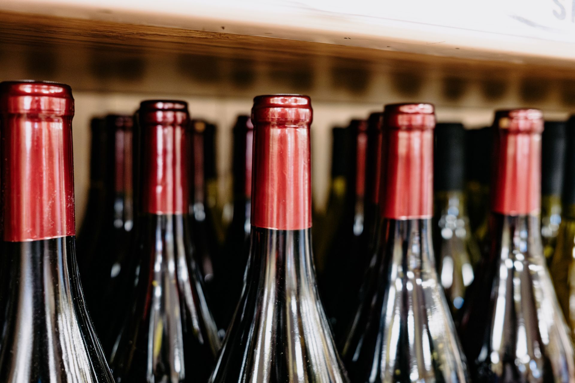 Bottiglie di vino con tappi di stagnola rossa esposte su uno scaffale di legno.