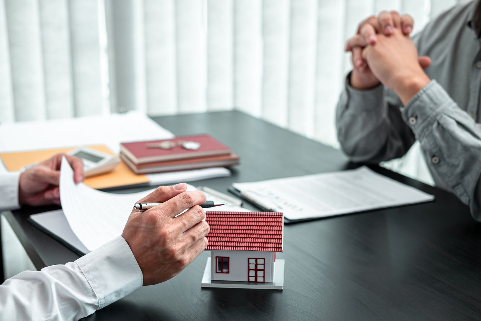 Real estate agent pointing to a contract; a small house model sits on the table as a man listens.