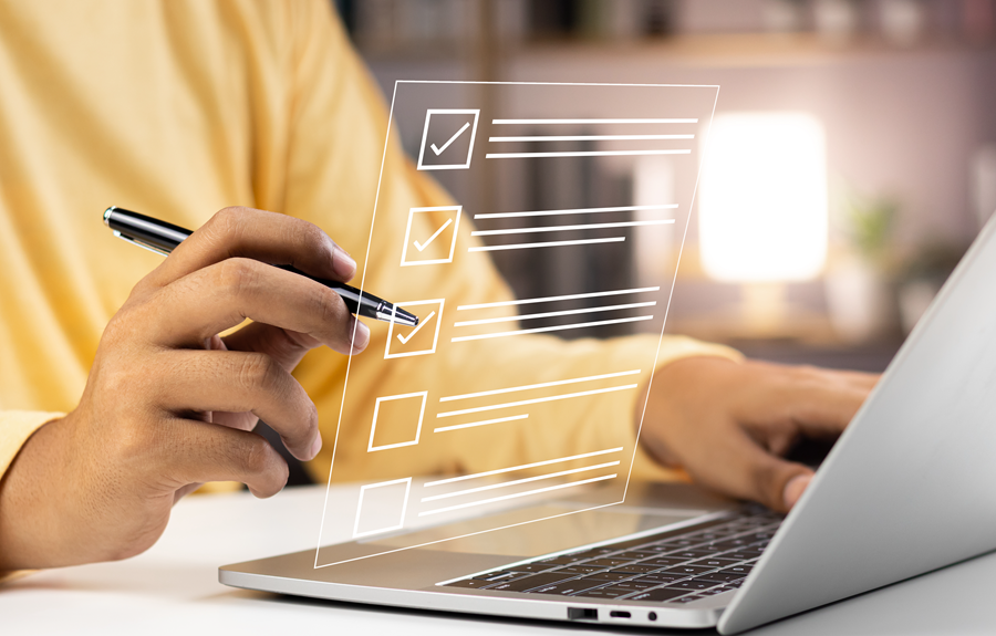 Hands typing on a laptop beside a checklist overlay in a warm, blurred office setting